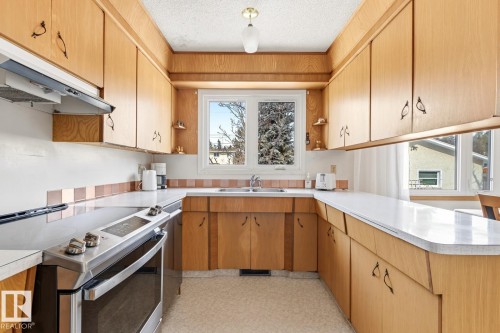 The kitchen features light wood cabinetry, white countertops, and a tile backsplash - 10716 52 Avenue, Edmonton, AB - Indoor Photo Showing Kitchen With Double Sink