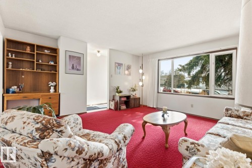 Bright living area featuring a large window, providing natural light, and a built-in wooden shelving unit - 10716 52 Avenue, Edmonton, AB - Indoor Photo Showing Living Room