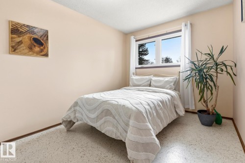 This inviting room features neutral-toned walls, a bed with a light-colored duvet, and a window providing natural light - 10716 52 Avenue, Edmonton, AB - Indoor Photo Showing Bedroom