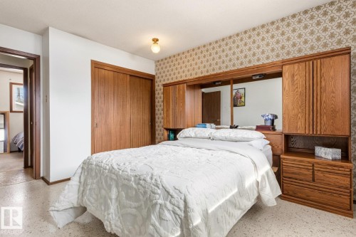 Bedroom featuring a built-in wooden headboard unit with integrated cabinetry, a sliding door closet, and patterned wallpaper - 10716 52 Avenue, Edmonton, AB - Indoor Photo Showing Bedroom