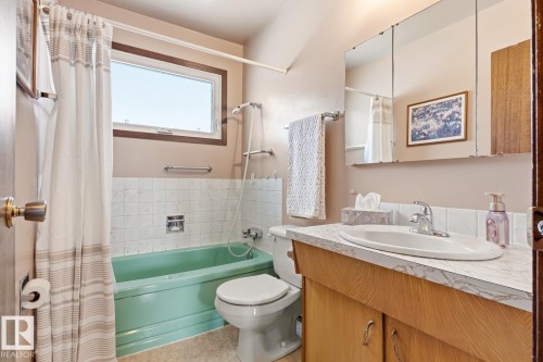 The bathroom features a vanity with a countertop and an integrated sink, a mirror, and a window - 10716 52 Avenue, Edmonton, AB - Indoor Photo Showing Bathroom