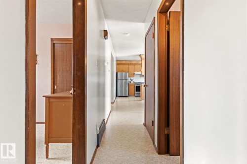 The property features a hallway with light-colored flooring and white walls, leading towards a kitchen with light wood cabinetry and a stainless steel refrigerator - 10716 52 Avenue, Edmonton, AB - Indoor Photo Showing Other Room