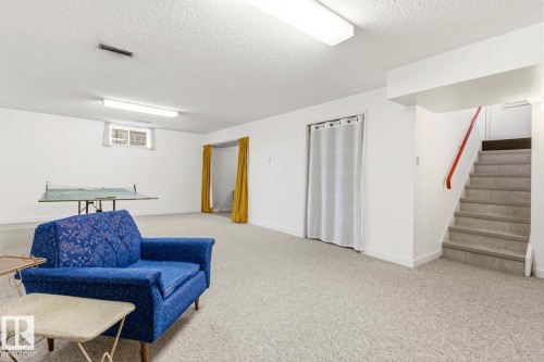 The property features a spacious room with light-colored carpeting, white walls, and overhead fluorescent lighting - 10716 52 Avenue, Edmonton, AB - Indoor