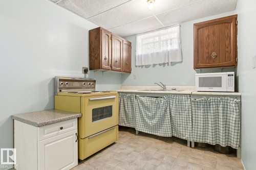 The kitchen features wood cabinetry, a yellow stove, a sink, and a microwave - 10716 52 Avenue, Edmonton, AB - Indoor Photo Showing Kitchen