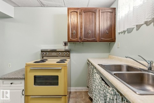 The kitchen features a double basin stainless steel sink, wood cabinetry, a range, and light-colored countertops - 10716 52 Avenue, Edmonton, AB - Indoor Photo Showing Kitchen With Double Sink