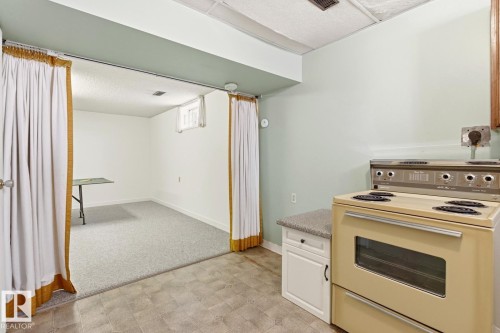 Kitchen area with a beige range and white base cabinet with a countertop, opening to a carpeted room with white walls and a window - 10716 52 Avenue, Edmonton, AB - Indoor Photo Showing Kitchen