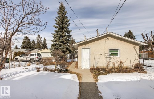 The property includes a detached structure with stucco siding and a white door, set on a lot with mature trees and a concrete pathway - 10716 52 Avenue, Edmonton, AB - Outdoor