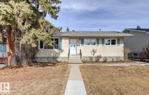 The property features a concrete walkway leading to the front entrance, a front yard with a lawn, and a mature evergreen tree - 10716 52 Avenue, Edmonton, AB - Outdoor