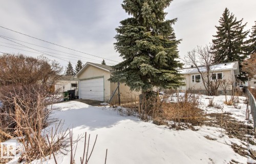 The property features a detached garage and a light-colored exterior, with mature trees visible on the grounds - 10716 52 Avenue, Edmonton, AB - Outdoor