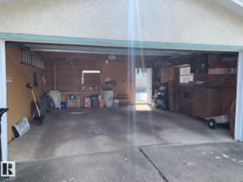 The property features a garage with an open overhead door, concrete flooring, and interior wooden walls - 10716 52 Avenue, Edmonton, AB - Indoor Photo Showing Garage