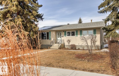 The property features a stucco exterior, a gray shingle roof, a front yard with a lawn, and mature trees surrounding the property - 10716 52 Avenue, Edmonton, AB - Outdoor