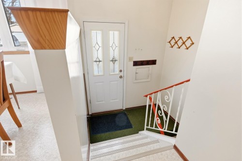 Entryway featuring a white door with decorative glass inserts, a built-in coat rack, and a staircase with a decorative white and orange railing - 10716 52 Avenue, Edmonton, AB - Indoor Photo Showing Other Room