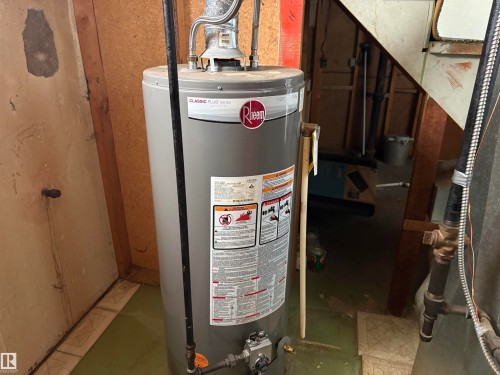 A Rheem Classic Plus Series water heater is installed, with exposed wood framing and a utility area visible - 10916 151 Street, Edmonton, AB - Indoor Photo Showing Basement