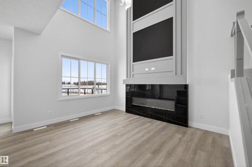 Living area with light-toned flooring, large windows, and a modern fireplace featuring a dark stone surround and a decorative mantel - 190 Elliott Wynd, Fort Saskatchewan, AB - Indoor With Fireplace