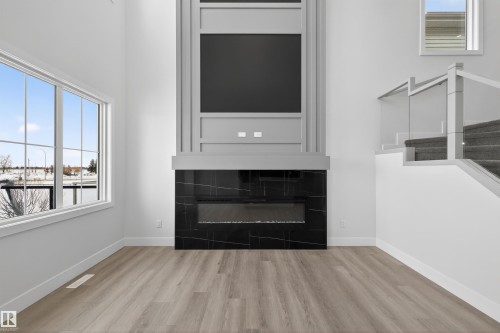 Living area featuring a modern fireplace with a black marble surround, high ceilings, large windows, and light wood-style flooring - 190 Elliott Wynd, Fort Saskatchewan, AB - Indoor Photo Showing Living Room With Fireplace