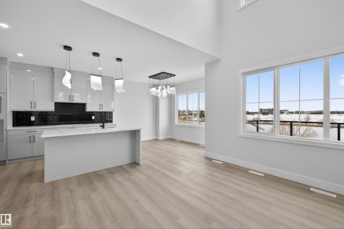This open-concept living space features light-toned flooring, high ceilings, and large windows offering exterior views - 190 Elliott Wynd, Fort Saskatchewan, AB - Indoor Photo Showing Kitchen