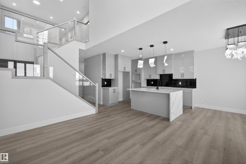 The open-concept living area features light-toned flooring, a kitchen with a central island and pendant lighting, and a modern glass-panel staircase - 190 Elliott Wynd, Fort Saskatchewan, AB - Indoor Photo Showing Kitchen