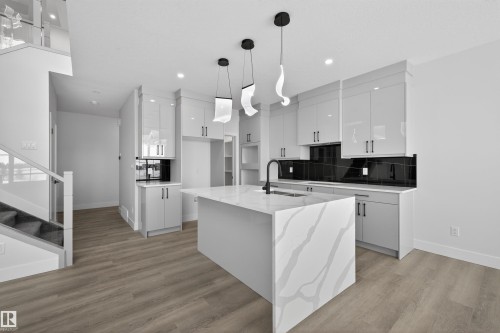 This kitchen features an island with a quartz countertop and integrated sink, sleek grey cabinetry, and a dark tile backsplash - 190 Elliott Wynd, Fort Saskatchewan, AB - Indoor Photo Showing Kitchen With Upgraded Kitchen