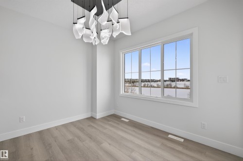 This room features light-colored walls, light wood-look flooring, and a contemporary ceiling light fixture - 190 Elliott Wynd, Fort Saskatchewan, AB - Indoor Photo Showing Other Room
