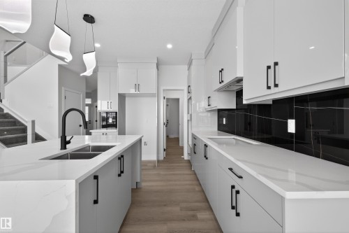 The kitchen features white cabinetry, white countertops, and a black marble-style backsplash - 190 Elliott Wynd, Fort Saskatchewan, AB - Indoor Photo Showing Kitchen With Double Sink With Upgraded Kitchen