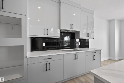 The kitchen features sleek grey cabinetry with black handles, a white countertop, and a black backsplash - 190 Elliott Wynd, Fort Saskatchewan, AB - Indoor Photo Showing Kitchen