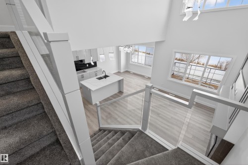 Two-story open concept living area featuring a kitchen island with a sink, light-colored flooring, and large windows - 190 Elliott Wynd, Fort Saskatchewan, AB - Indoor Photo Showing Other Room