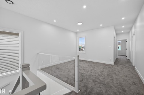 This bright landing area features recessed lighting, plush grey carpeting, and a modern glass and grey banister - 190 Elliott Wynd, Fort Saskatchewan, AB - Indoor Photo Showing Other Room
