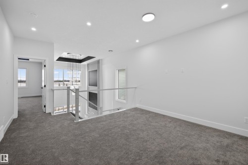 The upper level features plush carpeting, recessed lighting, and a modern glass railing overlooking the lower level - 190 Elliott Wynd, Fort Saskatchewan, AB - Indoor Photo Showing Other Room