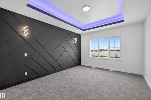 This room features a decorative accent wall with geometric paneling and integrated sconce lighting, complemented by a tray ceiling with recessed lighting - 190 Elliott Wynd, Fort Saskatchewan, AB - Indoor Photo Showing Other Room