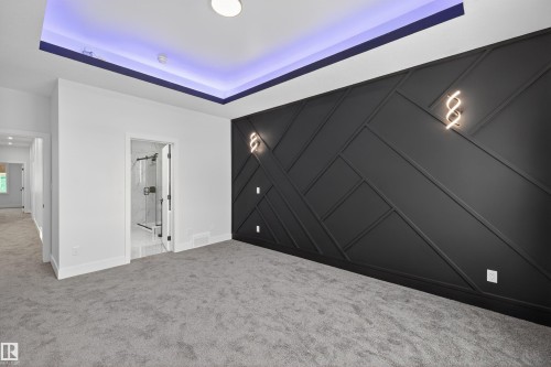 This room features a striking accent wall with geometric paneling, recessed ceiling lighting with a purple hue, and soft grey carpeting - 190 Elliott Wynd, Fort Saskatchewan, AB - Indoor Photo Showing Other Room