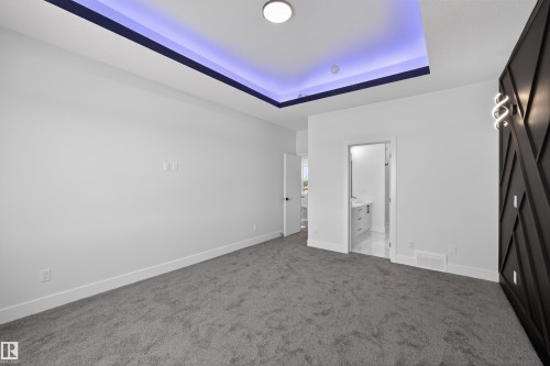 This room features a tray ceiling with accent lighting, a dark accent wall with decorative paneling and sconce lighting, and a view into a bathroom with a vanity - 190 Elliott Wynd, Fort Saskatchewan, AB - Indoor Photo Showing Other Room