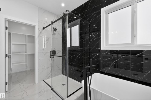 The bathroom features a spacious glass-enclosed shower with black fixtures and contrasting black and white marble-style tiling - 190 Elliott Wynd, Fort Saskatchewan, AB - Indoor Photo Showing Bathroom