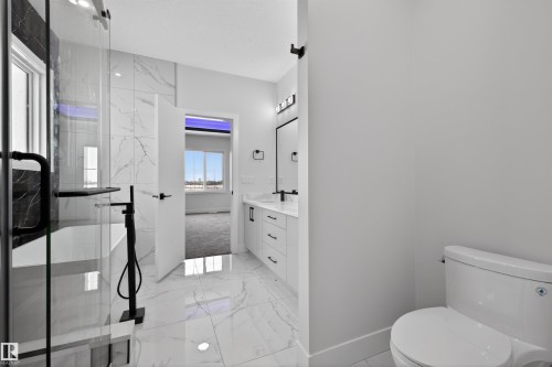 The bathroom features a modern freestanding bathtub with a matte black floor-mounted faucet, a glass-enclosed shower, and a vanity with a large mirror - 190 Elliott Wynd, Fort Saskatchewan, AB - Indoor Photo Showing Bathroom