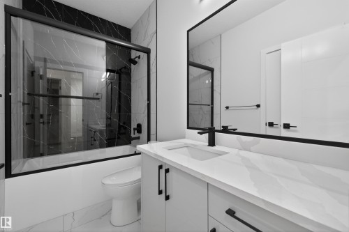 Bathroom featuring a bathtub with a clear glass enclosure, a white vanity with a white countertop, and a large mirror - 190 Elliott Wynd, Fort Saskatchewan, AB - Indoor Photo Showing Bathroom