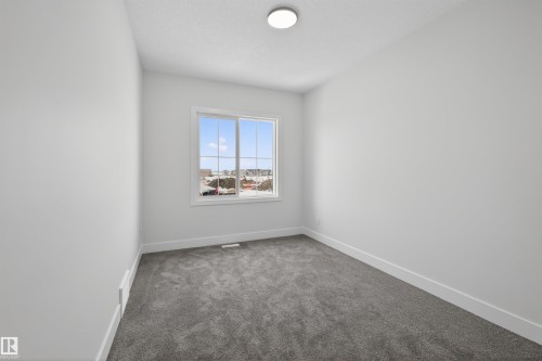 This bright room features a window providing natural light, a ceiling light fixture, and plush grey carpet flooring - 190 Elliott Wynd, Fort Saskatchewan, AB - Indoor Photo Showing Other Room