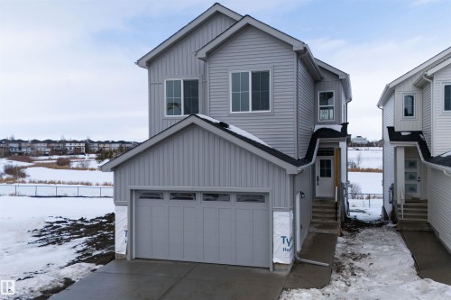This property features light gray siding, a prominent front-facing garage, and a concrete driveway - 190 Elliott Wynd, Fort Saskatchewan, AB - Outdoor