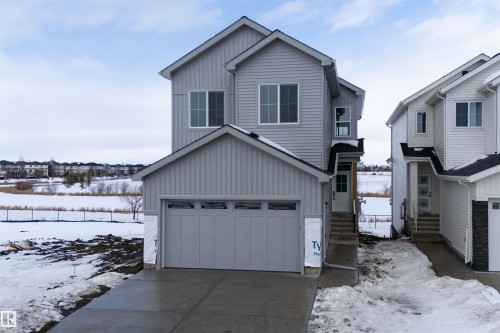 The property features light gray siding, a prominent attached garage with a concrete driveway, and a welcoming front entrance with steps - 190 Elliott Wynd, Fort Saskatchewan, AB - Outdoor