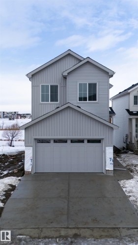 The property features a light grey exterior with vertical and horizontal siding, a two-car garage with panel detailing, and a concrete driveway - 190 Elliott Wynd, Fort Saskatchewan, AB - Outdoor