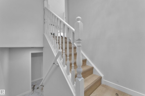 The property features a staircase with light wood treads, white risers, and a white balustrade with ornate newel posts - 5118 17A Ave, Edmonton, AB - Indoor Photo Showing Other Room