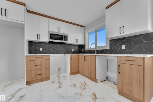 The kitchen features white upper cabinetry, light wood-toned lower cabinetry, a dark hexagonal tile backsplash, and a stainless steel microwave - 5118 17A Ave, Edmonton, AB - Indoor Photo Showing Kitchen