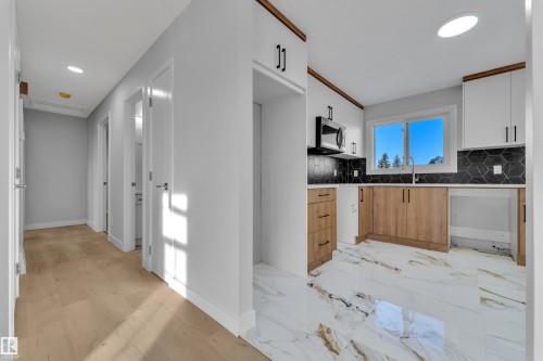 The kitchen features a window with natural light, white upper cabinets, wood tone lower cabinets, and black hexagonal tile backsplash - 5118 17A Ave, Edmonton, AB - Indoor Photo Showing Kitchen