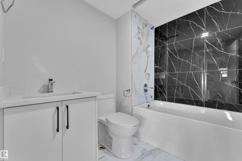 Bathroom featuring a toilet, bathtub with black marble-style wall tiles, and a vanity with a white countertop and chrome faucet - 5118 17A Ave, Edmonton, AB - Indoor Photo Showing Bathroom