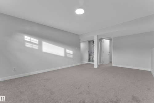 Spacious room featuring carpeting, light-colored walls, and an overhead light fixture, with a partial view of a toilet and a door opening into an additional area - 5118 17A Ave, Edmonton, AB - Indoor Photo Showing Other Room