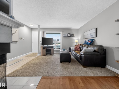 The living area features a large window, light gray walls, and a combination of carpet and wood flooring - 165 2703 79 Street, Edmonton, AB - Indoor Photo Showing Living Room