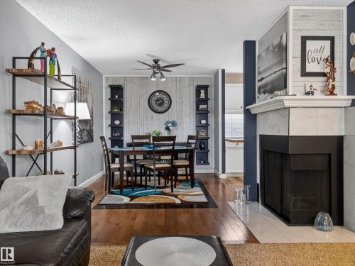 This living area features hardwood floors and a fireplace with a white mantel and black surround - 165 2703 79 Street, Edmonton, AB - Indoor With Fireplace