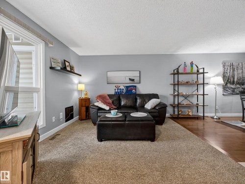 Living room featuring light-colored carpet, light blue walls, a large window, and a built-in shelving unit - 165 2703 79 Street, Edmonton, AB - Indoor