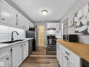 The kitchen features white cabinetry, a white subway tile backsplash, a double basin sink with a black faucet, and wood-look flooring - 165 2703 79 Street, Edmonton, AB  - Indoor Photo Showing Kitchen With Double Sink 