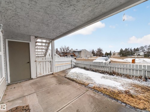The property features a concrete patio area with a white picket fence, offering views of the surrounding outdoor landscape and distant buildings - 165 2703 79 Street, Edmonton, AB - Outdoor With Exterior