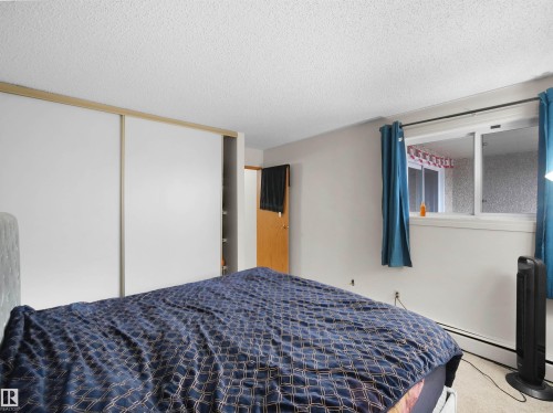 The room features a window with blue curtains and a ceiling with a textured finish - 214 2620 Mill Woods Road E, Edmonton, AB - Indoor Photo Showing Bedroom