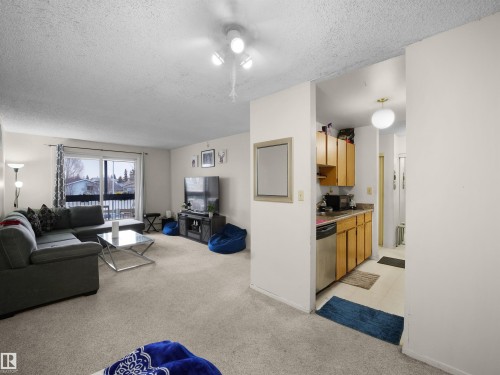 Living area featuring carpeted floors, a sliding glass door leading to an outdoor space, and an entryway to a kitchen with wood cabinetry and stainless steel appliances - 214 2620 Mill Woods Road E, Edmonton, AB - Indoor Photo Showing Living Room